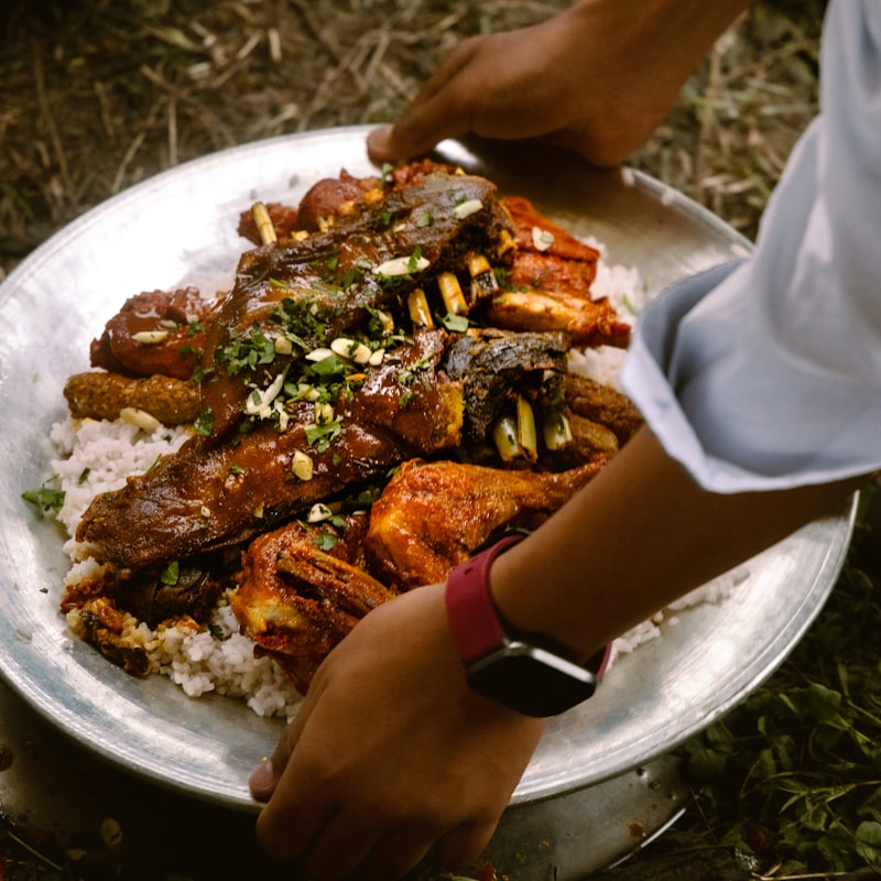 A steel platter of rice and slow-cooked meat being carried out to the table